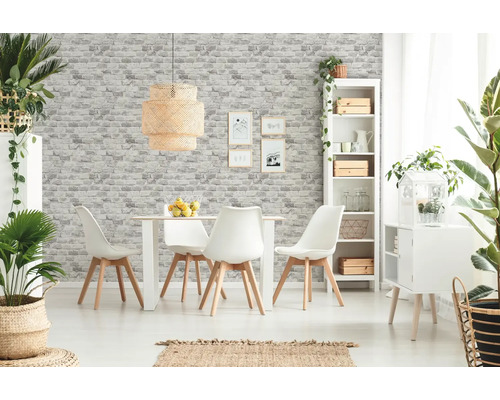Salle à manger lumineuse avec table, chaises, étagère et éléments décoratifs devant un mur avec du papier peint imitation pierre.
