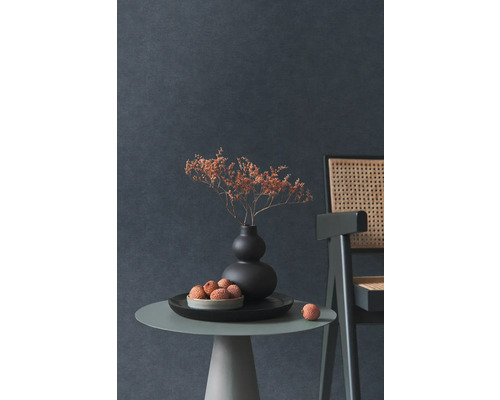 Dekoratives Stillleben mit Trockenblumen in Vase, Obstschale und Stuhl auf einem Beistelltisch vor einer dunklen Wand