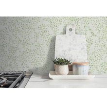 Mur décoratif à motif de feuilles, planche à découper, plante en pot et récipient sur une table de cuisine.
