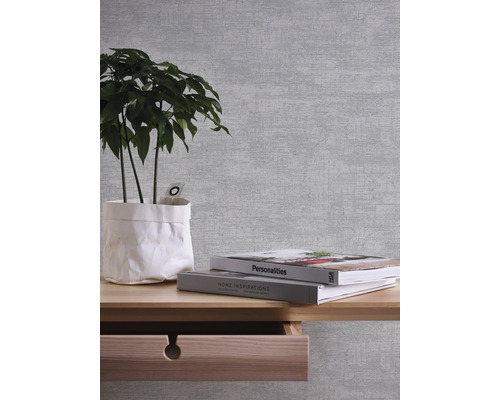 Nahaufnahme einer Wand mit Mustertapete, einem Holztisch, einer Zimmerpflanze und Büchern.