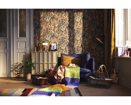 Wohnzimmer mit gemusterter Tapete, blauem Sessel und Strickdecke