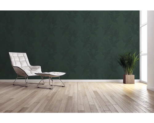 Wohnraum mit grüner Blättertapete, Sessel, Fußhocker, Topfpflanze und Holzboden