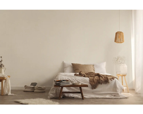 Helles Schlafzimmer mit Bett, Decke, Kissen, Beistelltisch, Lampe und dekorativen Elementen für eine freundliche Atmosphäre.