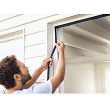 Une personne fixe un joint de fenêtre sur un cadre de fenêtre.