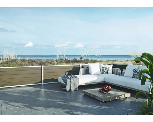 Moderne Terrasse mit hellgrauem Ecksofa für den Außenbereich, Holztisch und dunklen Bodenfliesen vor einer Küstenlandschaft mit Meerblick.