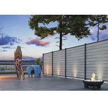 Moderne Terrasse mit grauem Sichtschutzzaun, Lounge-Möbeln und Feuerschale am Abend.