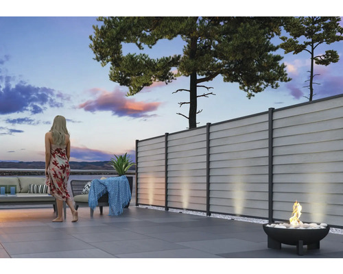 Moderne Terrasse mit grauem Sichtschutzzaun, Lounge-Möbeln und Feuerschale am Abend.