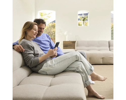 Un couple est assis sur un canapé et regarde un téléphone portable dans un salon lumineux.