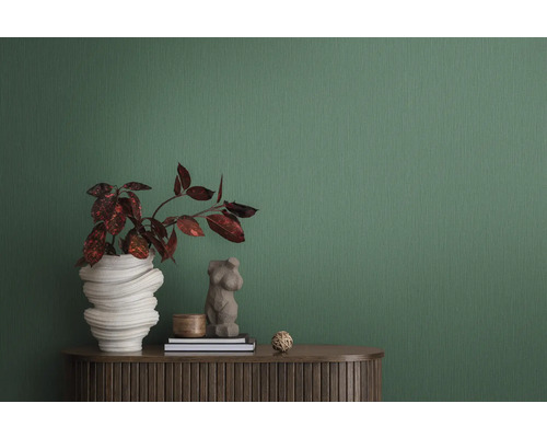 Scène d''intérieur décorative avec plante dans un vase sculptural, buste de femme et deux livres sur un meuble marron devant un papier peint vert