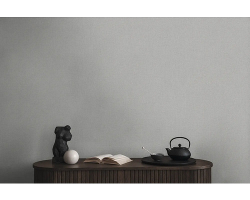 Dekoratives Stillleben mit Teekanne, Buch und Skulptur auf einem Holzschrank vor einer einfarbigen Wand.