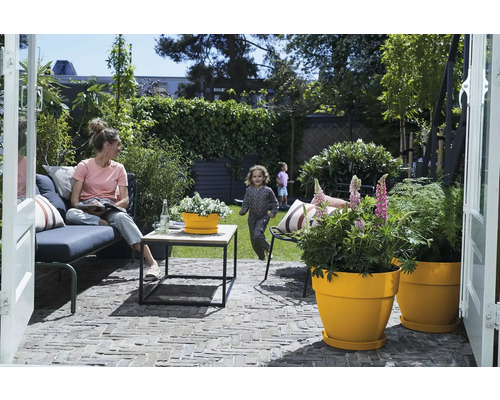 Terrasse mit Gartenmöbeln, Pflanzgefäßen und spielenden Kindern im Hintergrund