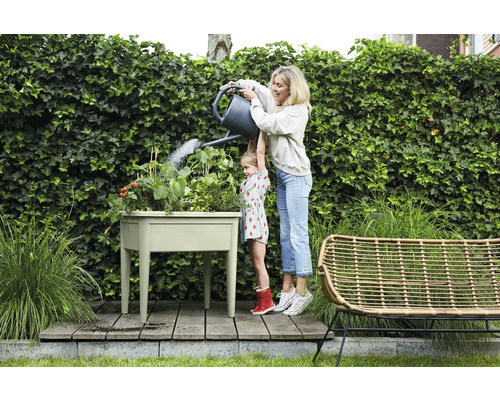 Eine Frau giesst mit ihrer Tochter einen Kräutergarten in einem Hochbeet im Garten.