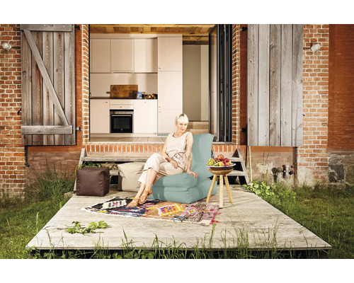 Eine Frau sitzt auf einem Sitzsack auf einer Terrasse vor einem Haus mit offener Küche.