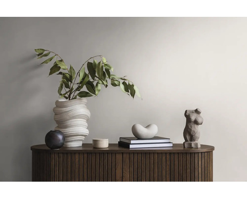 Dekorative Gegenstände auf einem Holzschrank: eine Vase mit Pflanzen, eine runde Dose, Bücher mit einer herzförmigen Figur und eine Frauenstatuette.