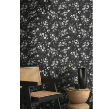 Vue d''une pièce avec un papier peint à motif de plantes d''eucalyptus derrière une chaise en bois et une table d''appoint.