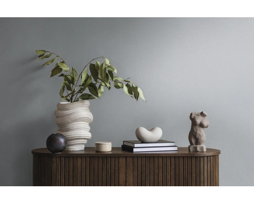 Dekorative Anordnung auf einem Holzschrank mit Vase, Grünpflanzen, Büchern und Skulpturen.