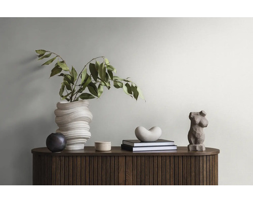 Arrangement décoratif avec vase, plantes, livres et sculptures sur une armoire en bois