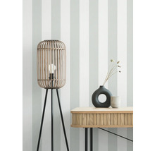 Lampadaire en bambou à trois pieds et table avec décoration devant un mur rayé