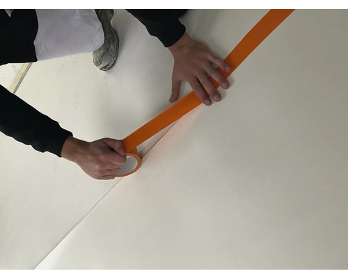 Une personne colle du ruban de masquage sur un sol pour délimiter une zone.