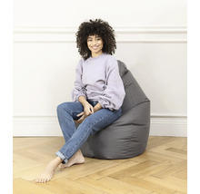 Femme assise sur un pouf gris dans une pièce lumineuse.