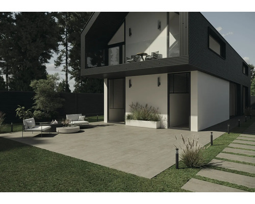 Außenbereich eines modernen Hauses mit Terrassenplatten, Rasenfläche und Gartenmöbeln.