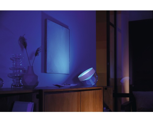 Szene mit einem Nachttisch, auf dem eine Lampe steht, die blaues Licht ausstrahlt, einem Bild an der Wand und einigen dekorativen Elementen.