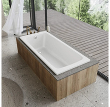 Baignoire blanche avec habillage en bois devant une fenêtre donnant sur des arbres