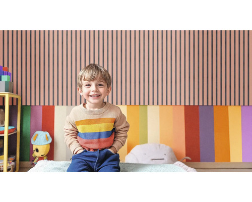 Ein Kind steht vor einer Wand mit vertikalen Streifen in einem Kinderzimmer.