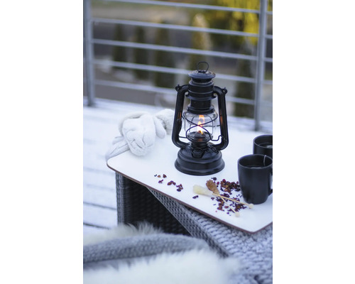Nature morte avec lampe à pétrole, gants et boissons sur une table à l''extérieur.