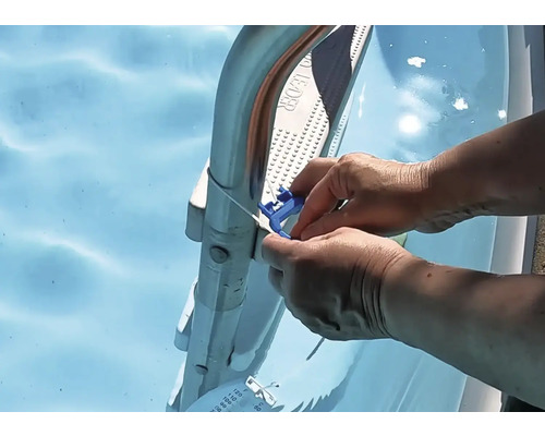 Une personne fixe un thermomètre bleu avec un câble sur une échelle de piscine