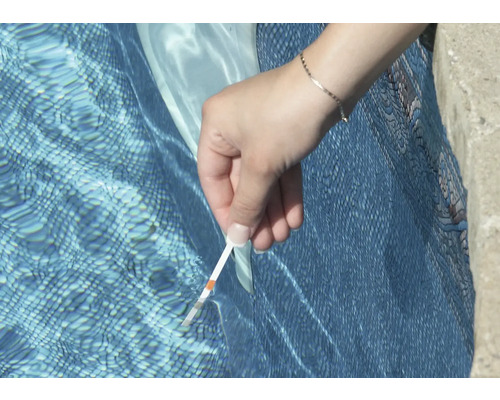 Une personne teste l''eau de la piscine avec une bandelette de test