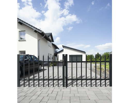 Toranlage aus Metall vor einem Wohnhaus mit gepflasterter Einfahrt.