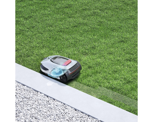 Robot tondeuse à gazon sur une pelouse près d''une bordure en pierre