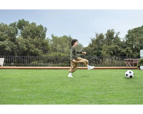 Un garçon joue au football sur une pelouse synthétique dans le jardin.