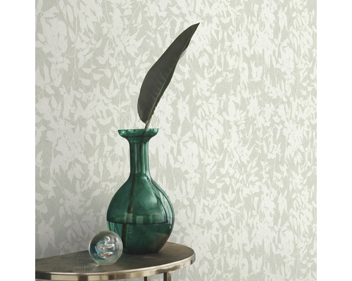 Tapete mit Blattmuster, kombiniert mit grüner Glasvase und dekorativer Glaskugel auf einem Tisch.