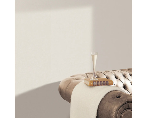 Detailaufnahme eines beigen Sofas mit gesteppter Oberfläche, auf dem sich ein Buch, eine helle Decke und ein Sektglas befinden.