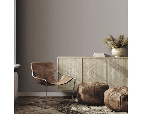 Wohnzimmer mit braunem Ledersessel, Kommode mit Muster und Poufs auf einem Teppich