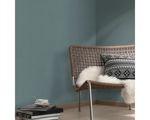 Wohnraumszene mit Rattan-Stuhl, Kissen und gemusterter Tapete.