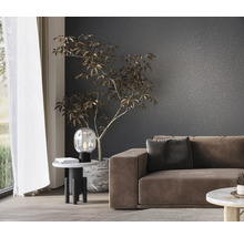 Wohnzimmer mit Sofa, Tischlampe und Zimmerpflanze vor einer gemusterten Wand