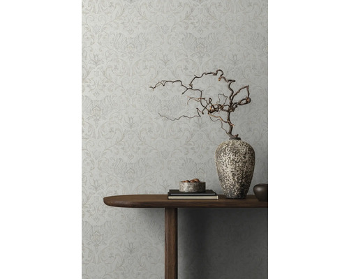 Detailansicht einer dekorierten Wand mit floral gemusterter Tapete, einem Holztisch mit Dekorationsgegenständen und einer Vase mit Zweigen.