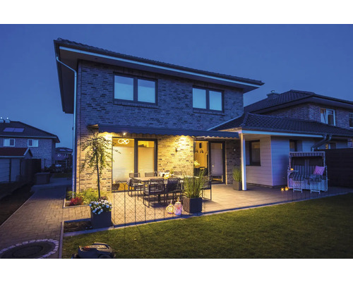 Maison avec terrasse, mobilier de jardin, store et robot tondeuse au crépuscule