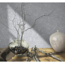 Arrangement décoratif avec vase, branches et pierres décoratives sur une table en bois devant un mur structuré.