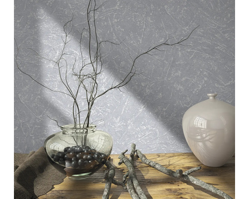 Arrangement décoratif avec vase, branches et pierres décoratives sur une table en bois devant un mur structuré.