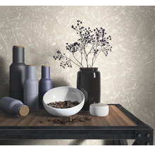 Scène décorative avec vases, bol et branches sur une table devant un papier peint mural.