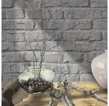 Branches décoratives dans un vase en verre sur une table en bois devant un mur de briques