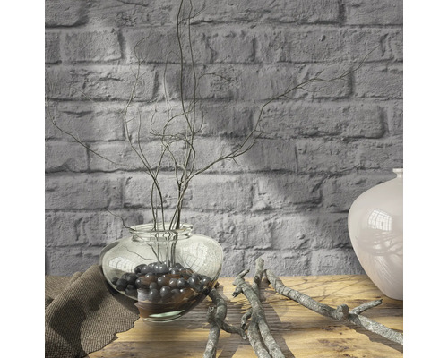 Branches décoratives dans un vase en verre sur une table en bois devant un mur de briques