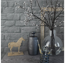 Scène décorative avec vase, branches, figurine de cheval et récipient avec des pinceaux sur une table devant un mur de briques