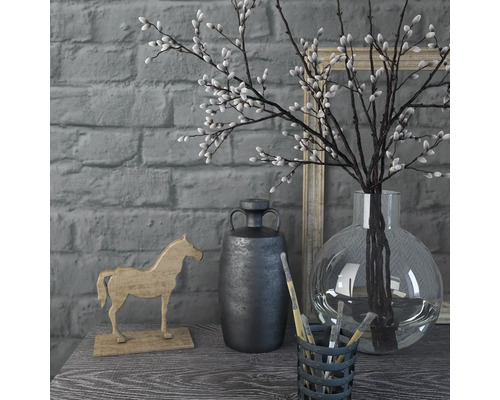 Scène décorative avec vase, branches, figurine de cheval et récipient avec des pinceaux sur une table devant un mur de briques