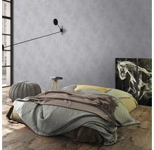 Schlafzimmer mit Bett, Nachttisch, Hocker und Wandleuchte vor grauer Wand