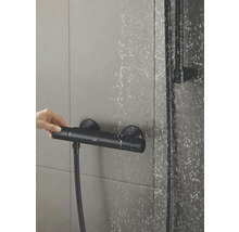 Aufnahme einer laufenden, montierten Duscharmatur mit Hand, Brausestange und fallenden Wassertropfen.